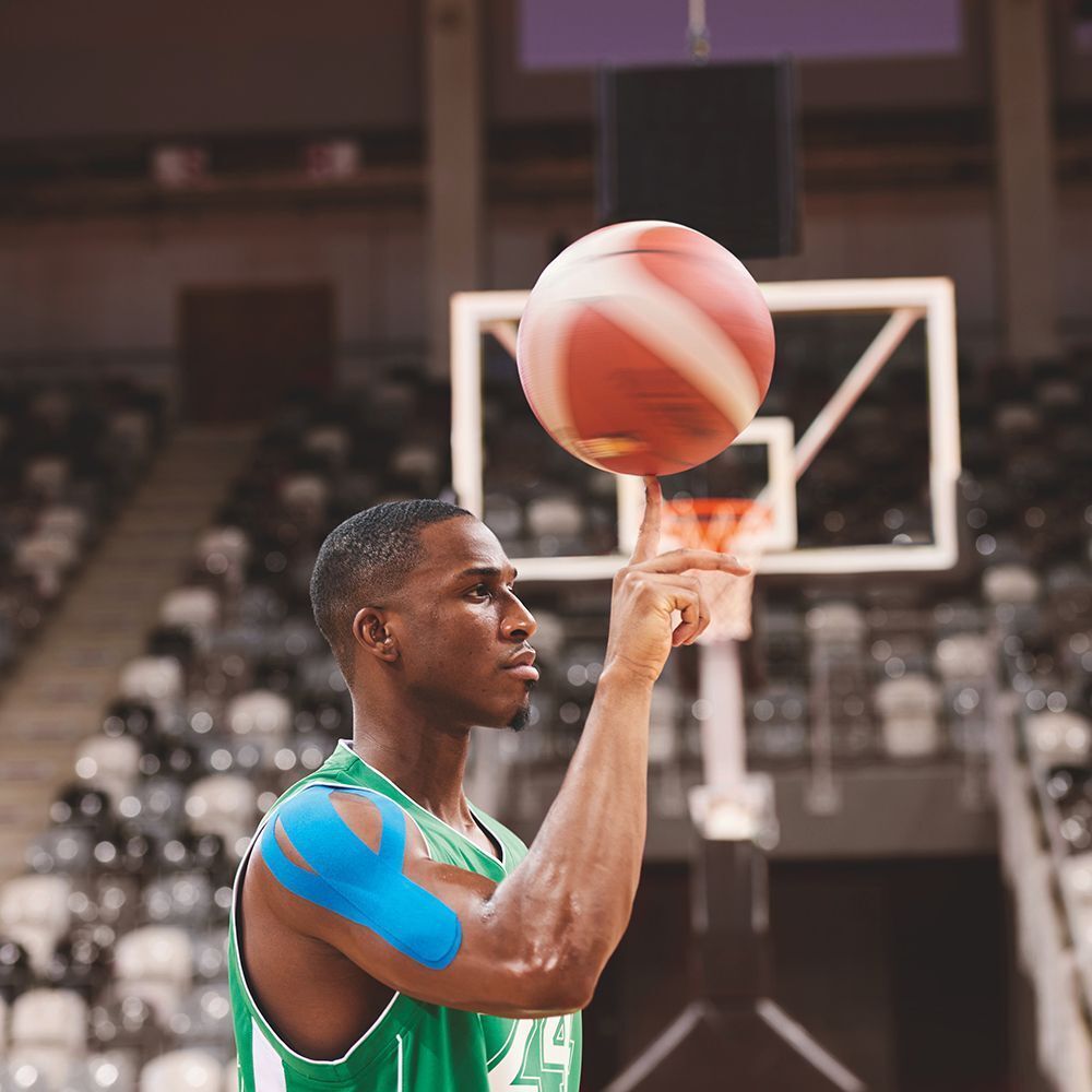 Un giocatore di basket con nastro kinesiologico blu sulla spalla, che palleggia.