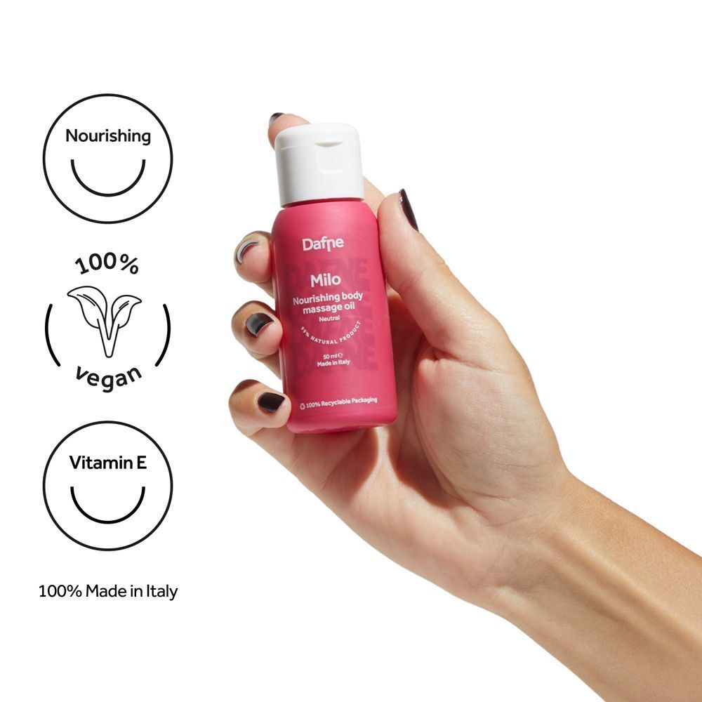 Mano che tiene una piccola bottiglia rosa di olio corpo Dafne Milo. Icone vegan, vitamina E, 100% Made in Italy.