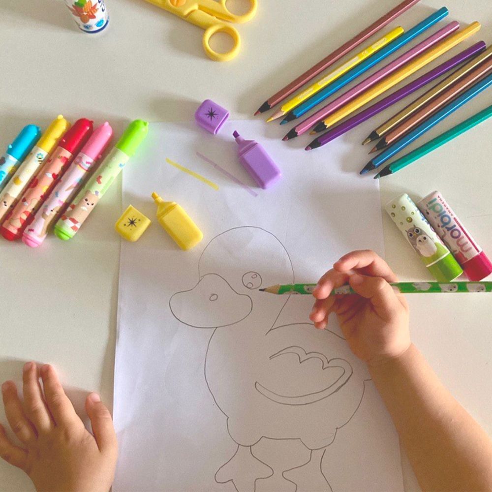 Un bambino disegna un'anatra, circondato da matite, pennarelli e stick labbra Morbidi.