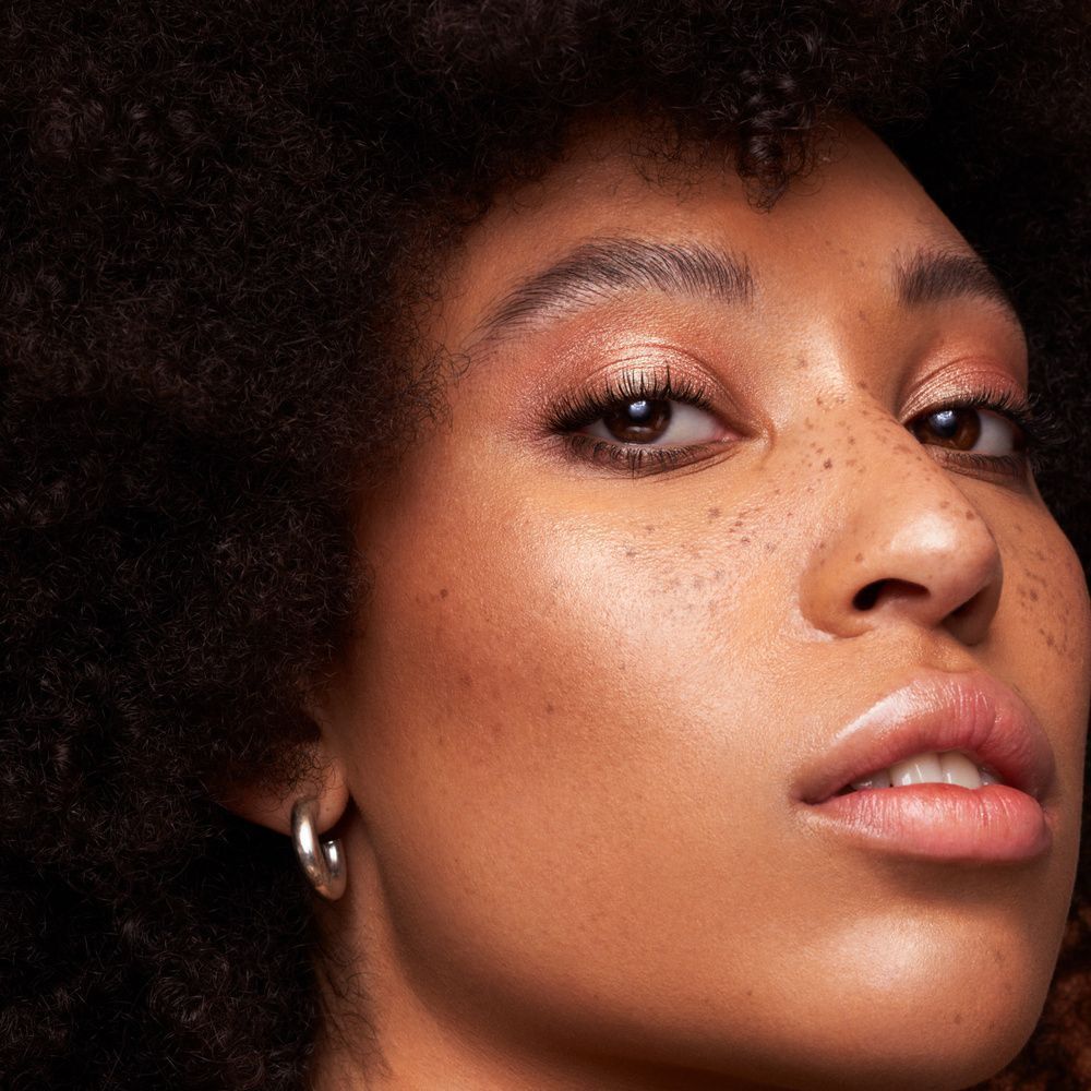 Primo piano di una donna con lentiggini e trucco luminoso.