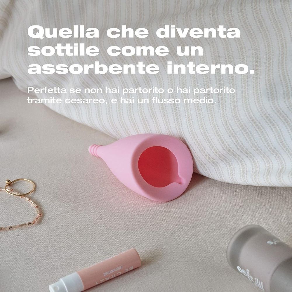 Coppetta mestruale rosa su sfondo di tessuto.