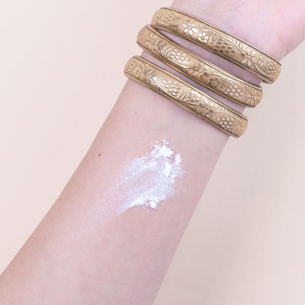 Un braccio con tre bracciali dorati e una macchia di polvere bianca sulla pelle.