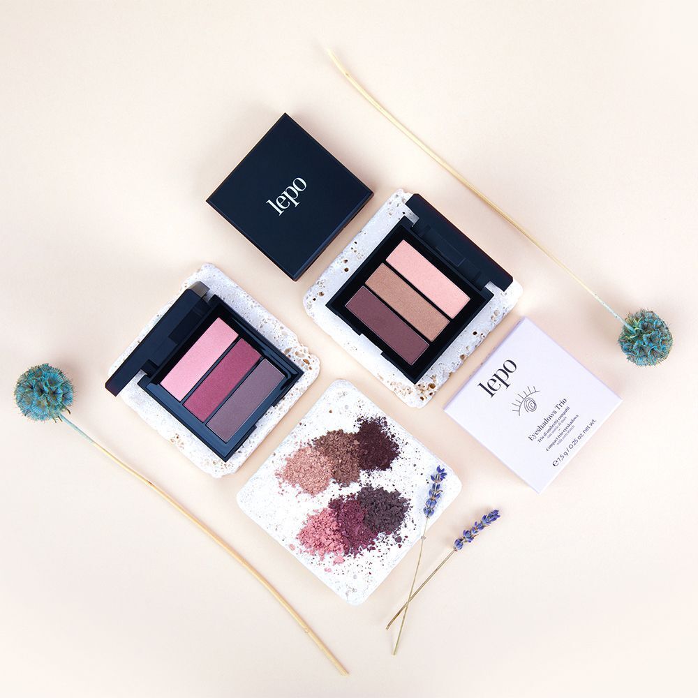 Due palette di ombretti Lepo, ciascuna con tre colori. Una palette mostra tonalità rosa e rosse, l'altra tonalità marroni e rosa. Accanto, polveri di ombretto in vari colori.