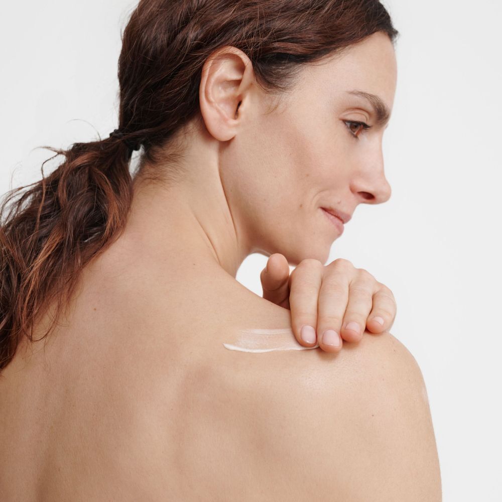Una donna applica una piccola quantità di crema bianca sulla spalla.