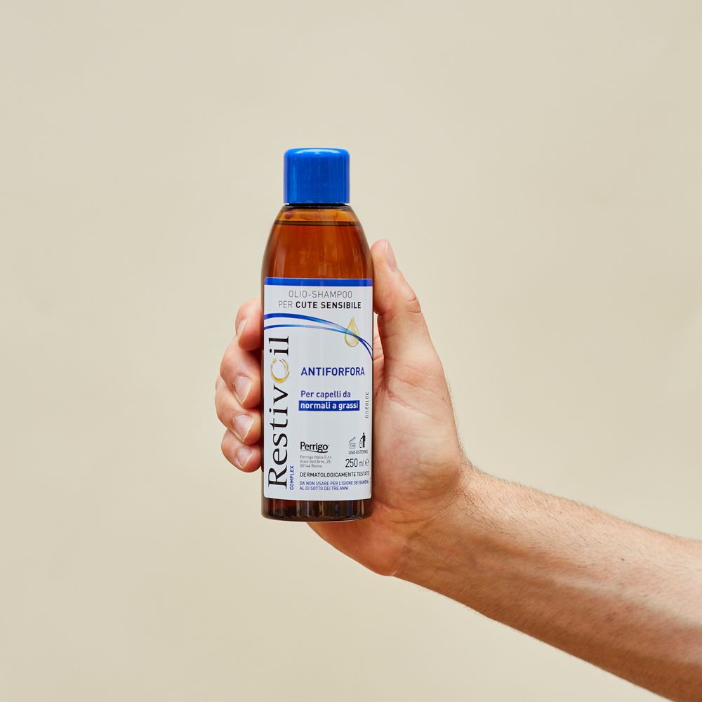 Eine Hand hält eine Flasche Restivoil Öl-Shampoo gegen Schuppen für empfindliche Kopfhaut.