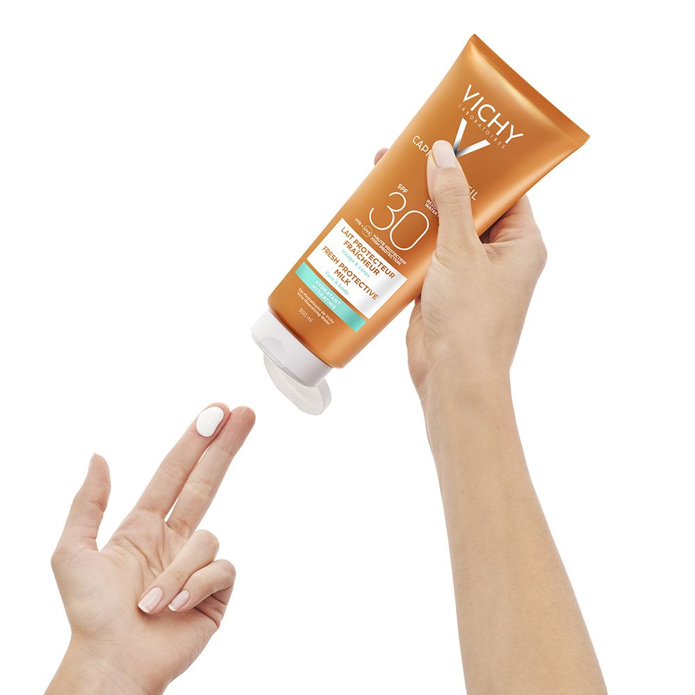 Mani che tengono un tubo di latte solare arancione e premono il latte solare su un dito.