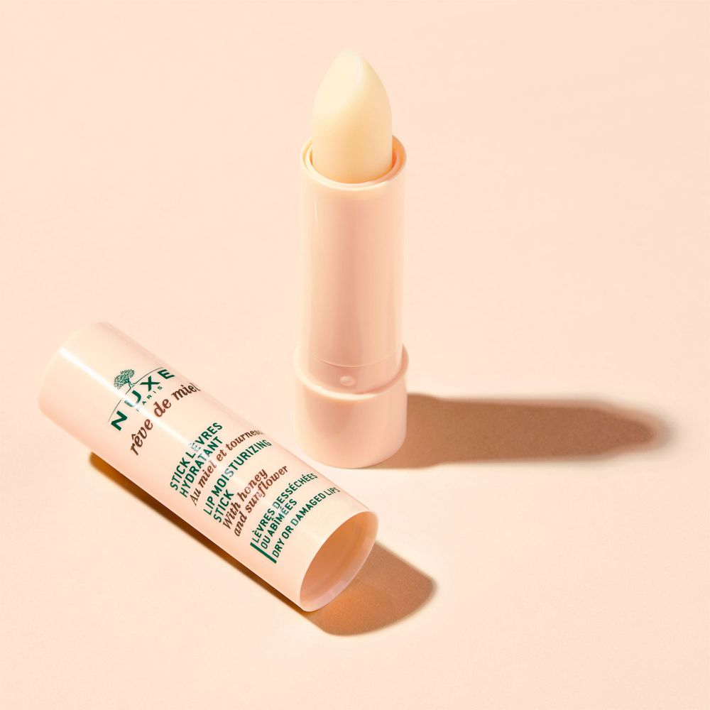 Stick labbra NUXE Rêve de Miel aperto. Tubetto e stick beige. Punta gialla chiara. Su sfondo chiaro.