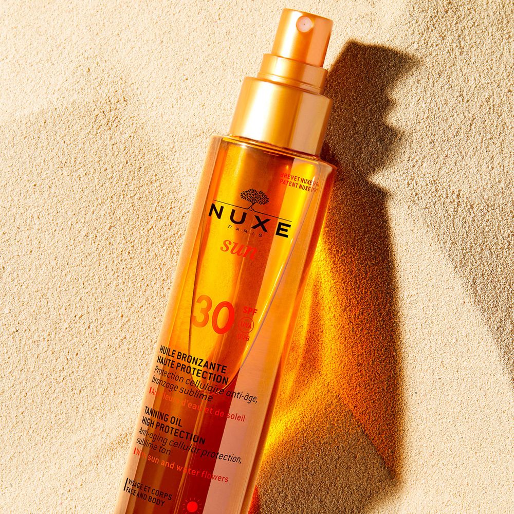 Olio abbronzante Nuxe Sun su sabbia. Flacone con tappo dorato e vaporizzatore.