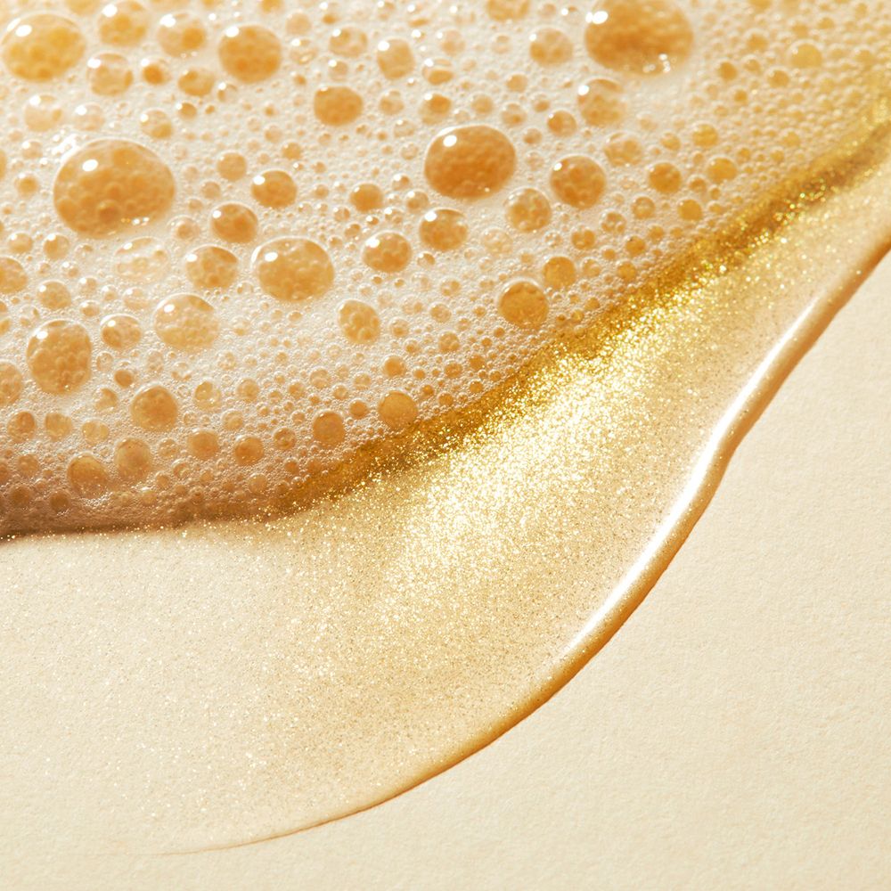 Nahaufnahme von goldfarbenem Duschöl mit Schaumbläschen. Flüssigkeit mit Schimmer.
