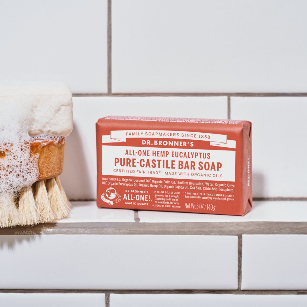 Sapone in barra accanto a una spazzola con schiuma. Confezione rossa con scritta: Dr. Bronner's, All-One Hemp Eucalyptus.