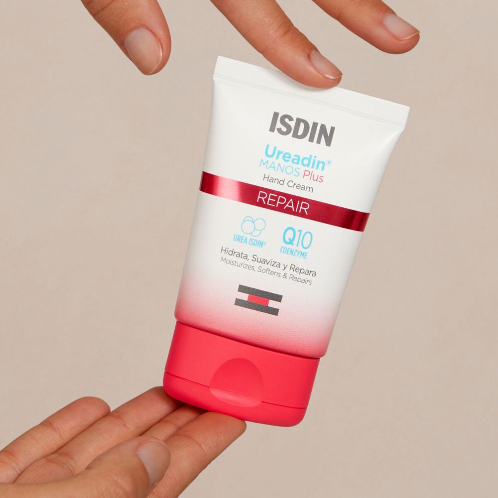 Mani che tengono un tubetto di crema per le mani. Scritta: ISDIN Ureadin® MANOS PLUS Hand Cream REPAIR.