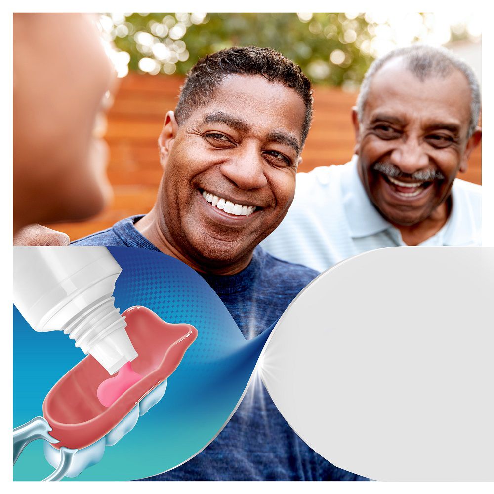Zwei Männer lachen, im unteren Bereich wird ein Haftmittel auf eine Zahnprothese aufgetragen.