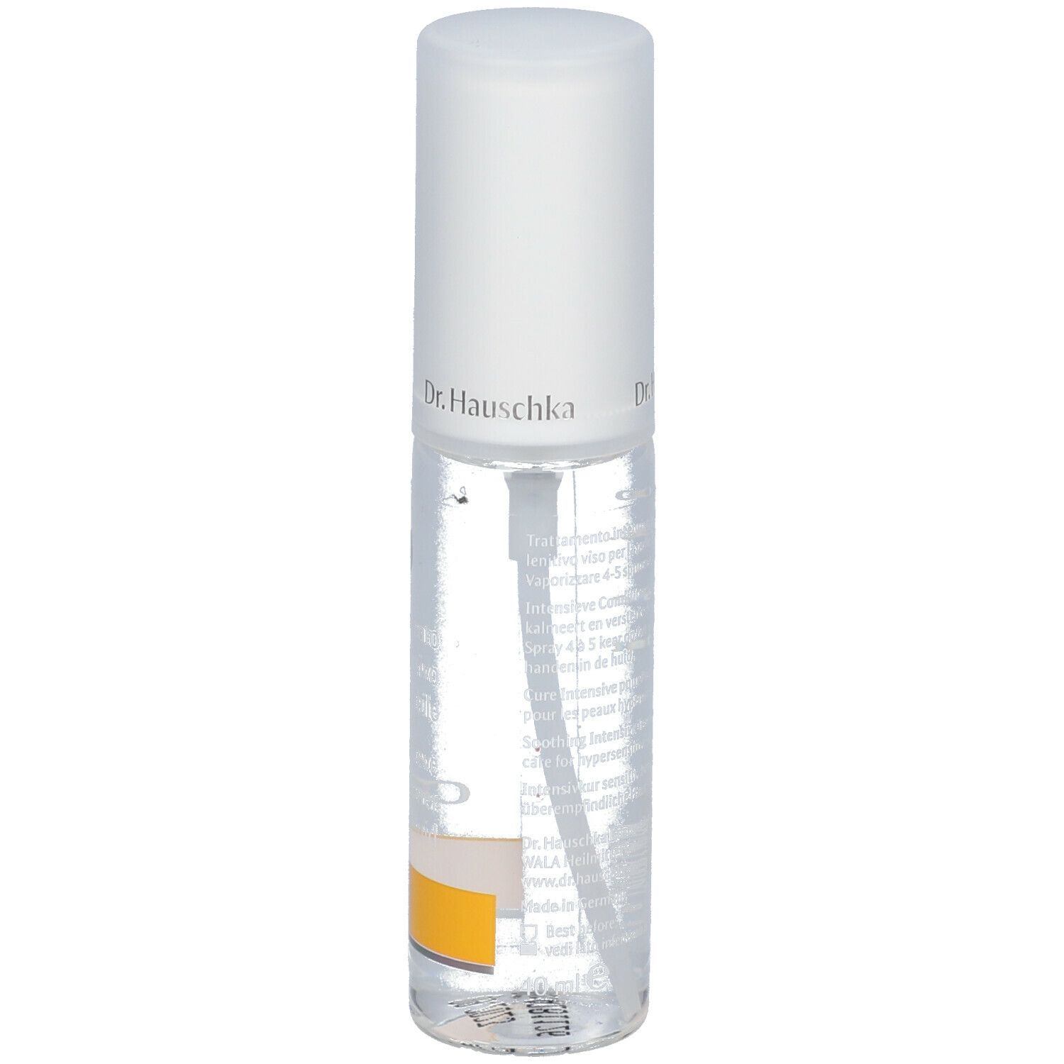 Flacone trasparente con erogatore spray. Scritta: Dr. Hauschka. Etichetta con testo. Striscia gialla in basso.