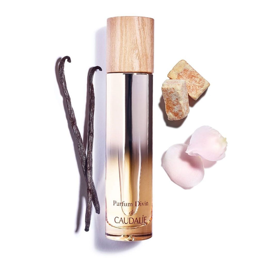 Flacone Parfum Divin con tappo in legno. Baccelli di vaniglia, petali e pezzi di zenzero accanto.