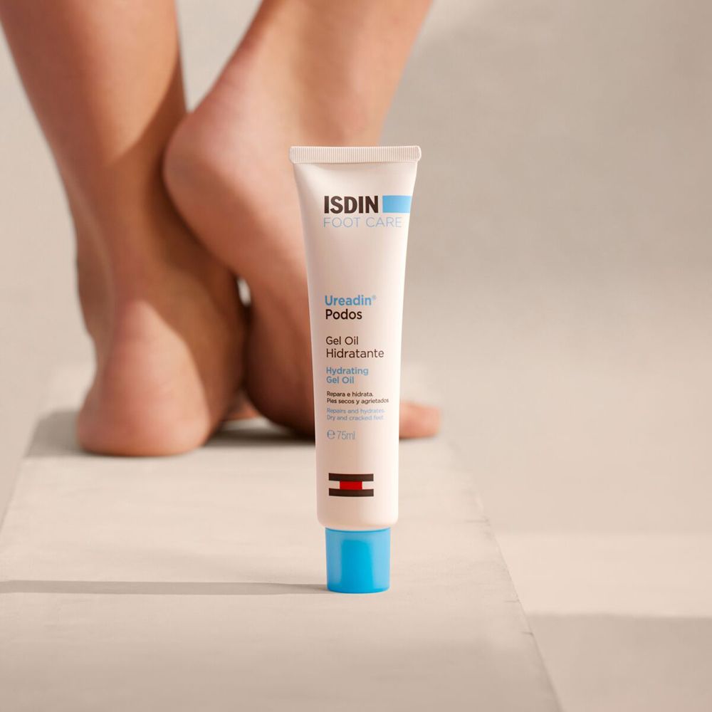 Tube de ISDIN Foot Care Ureadin Podos Gel Oil à côté de pieds. L'arrière-plan est flou.