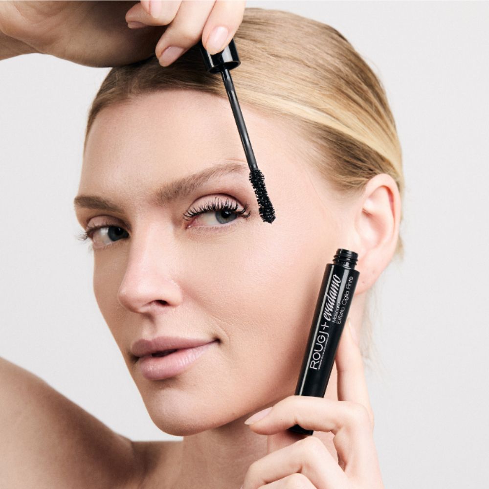 Frau wendet schwarze Mascara an, hält Tube und Applikator.