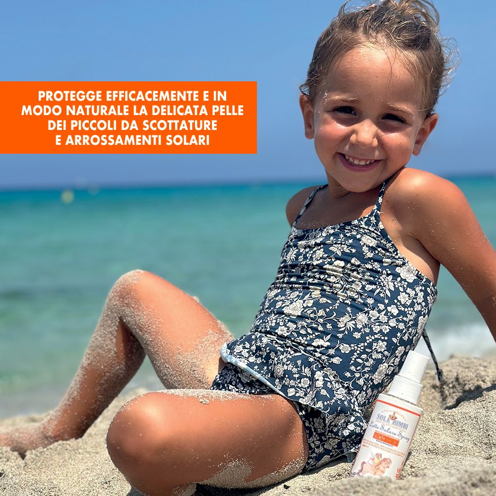 Kind am Strand mit Sonnenspray. Weiße Flasche mit orangefarbenem Etikett. Aufdruck: Sole Bimbi, SPF 50+.