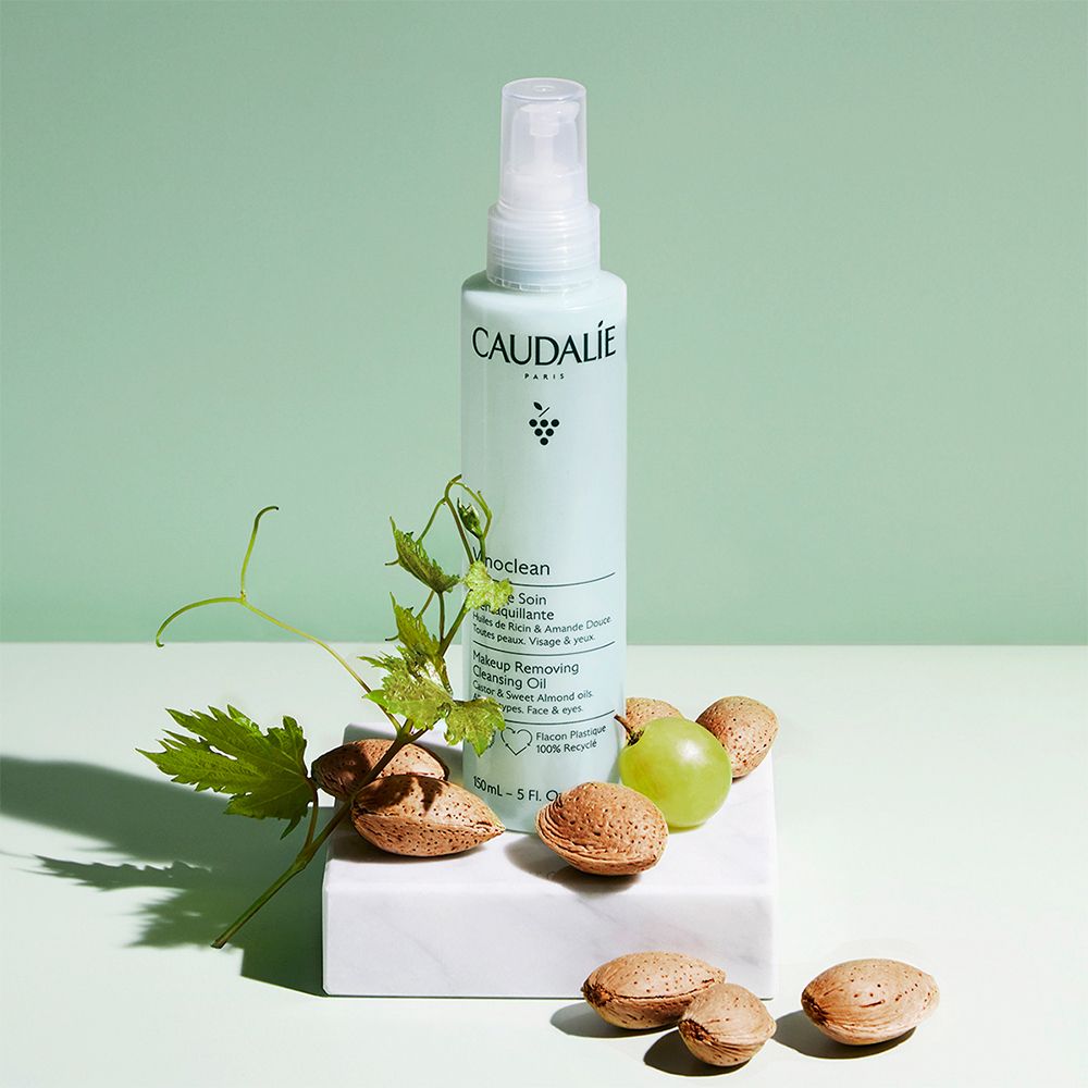 Flacone verde Caudalie Vinoclean con mandorle, uva e foglie su piedistallo bianco.