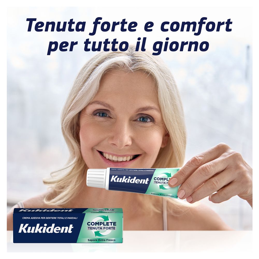 Frau hält Kukident-Tube. Aufschrift: Kukident, COMPLETE, Tenuta Forte, Sapore Extra Fresco. Frau lächelt. Hintergrund: weiß.