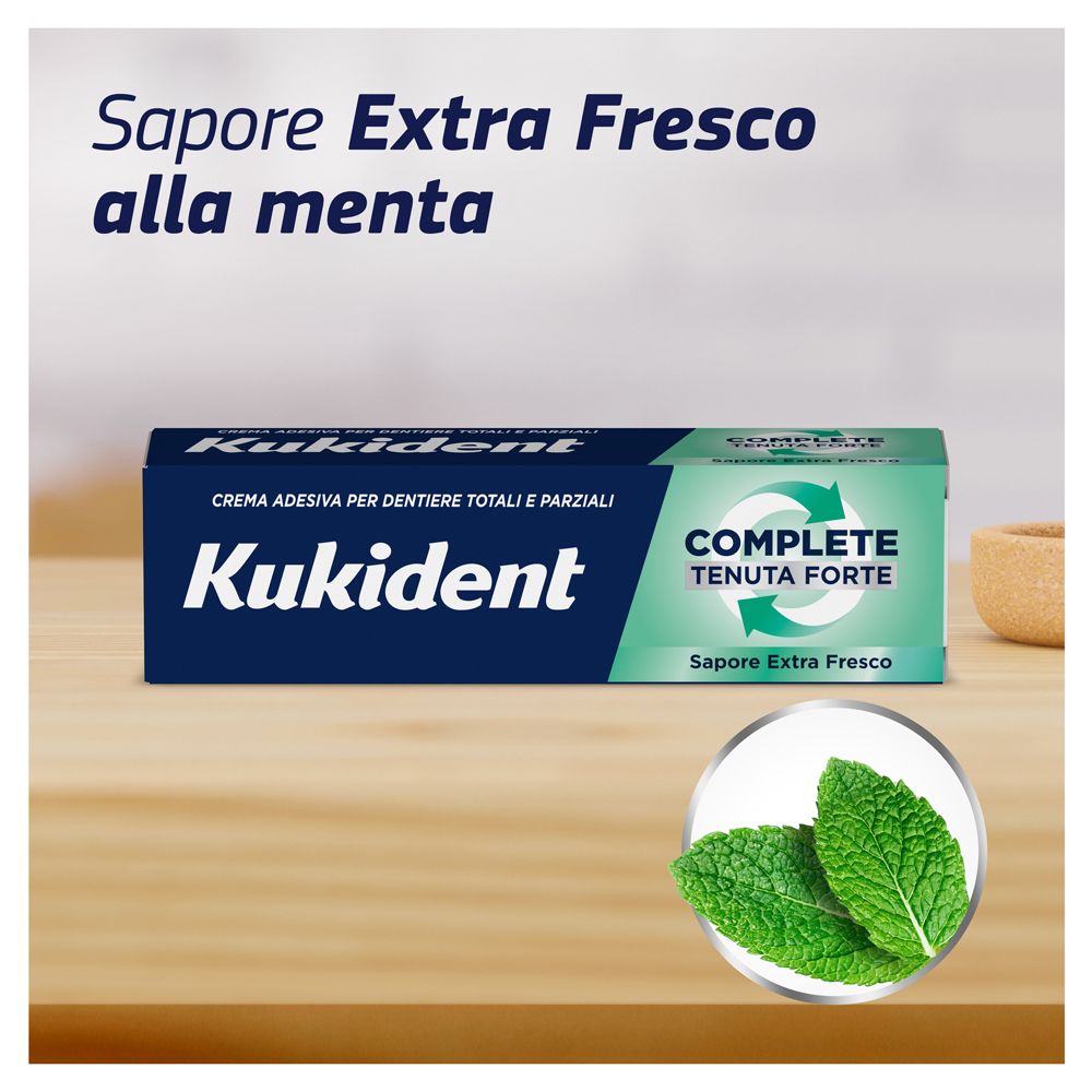 Kukident-Verpackung. Aufschrift: Kukident, COMPLETE, Tenuta Forte, Sapore Extra Fresco. Zwei Minzblätter. Hintergrund: Holz.