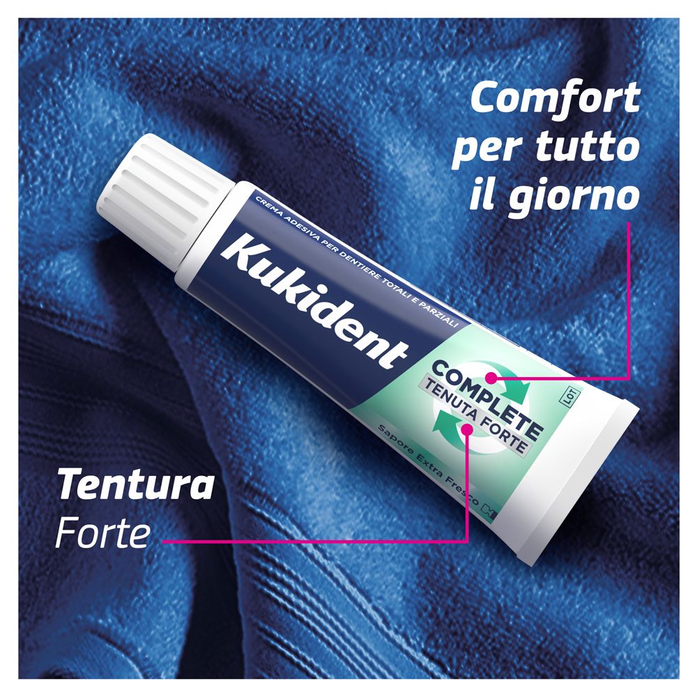 Kukident-Tube auf blauem Handtuch. Aufschrift: Kukident, COMPLETE, Tenuta Forte, Sapore Extra Fresco. Pinke Linien.