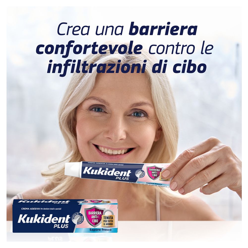 Frau hält eine Tube Kukident Plus Barriera Anti-Cibo Fresco. Auf dem Tisch liegt eine Schachtel. Text: Crea una barriera...