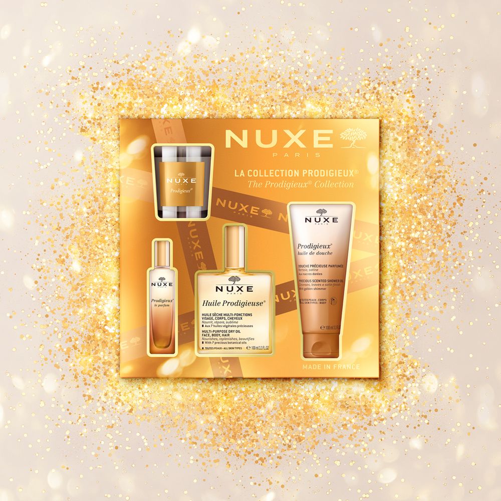 Confezione regalo Nuxe con olio, crema, gel doccia e candela. Confezione dorata. Logo Nuxe e nomi dei prodotti visibili.