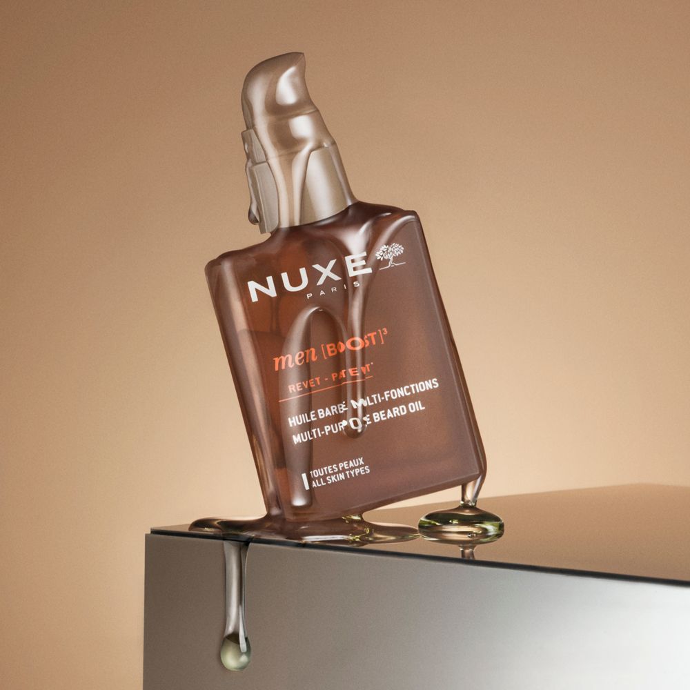 Braune Flasche mit Pumpe, Öl läuft heraus. Aufschrift: NUXE PARIS, men [BOOST] brevet - patent. Multi-Purpose Beard Oil.