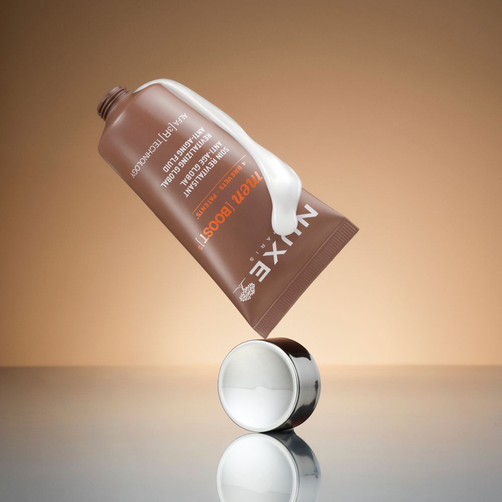 Tubo marrone con tappo argentato, prodotto accanto. Prodotto con crema bianca. Scritte: Nuxe, men Boost, Anti-Aging Fluid.
