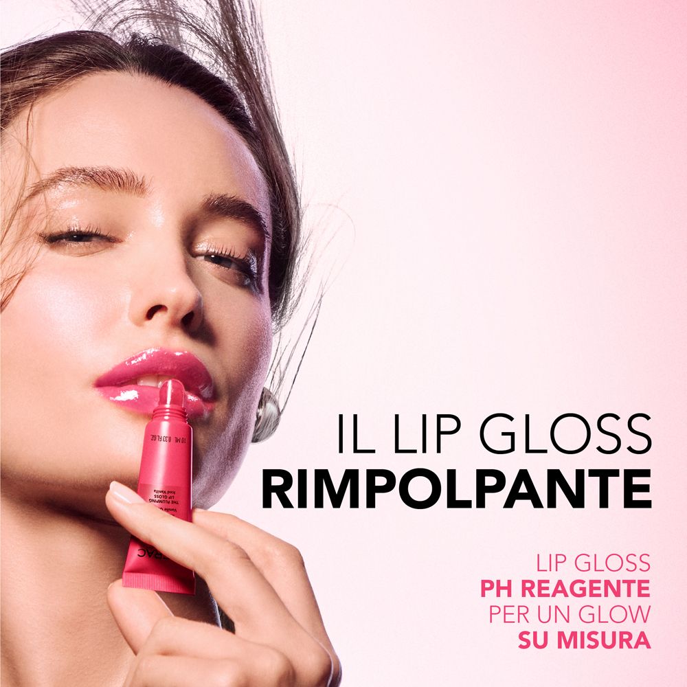 Una donna con labbra piene tiene in mano un piccolo tubetto di lucidalabbra rosa.