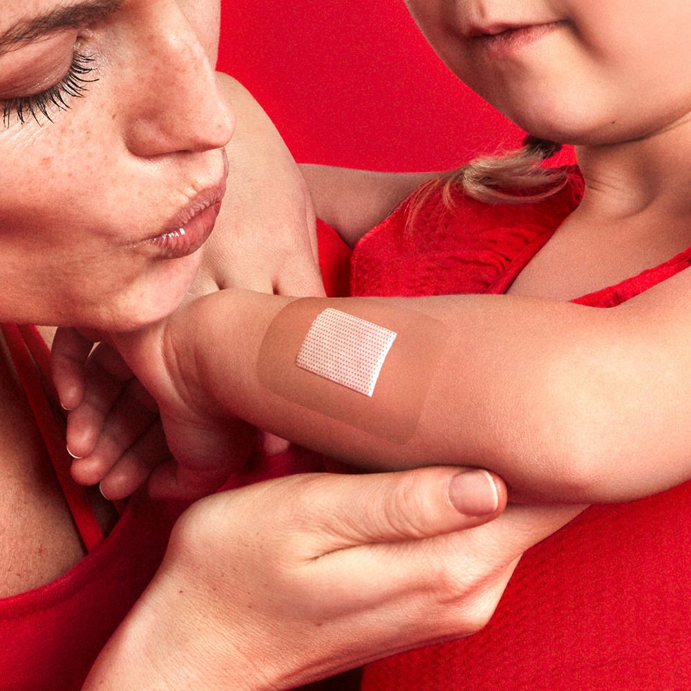 Arm eines Kindes mit einem Pflaster. Mutter hält Arm. Pflaster ist transparent.