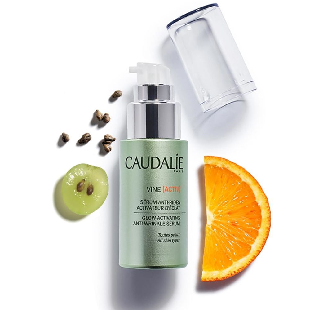 Flacone di siero verde con pompa, accanto uva, semi e fetta d'arancia. Scritta CAUDALIE VINE [ACTIV].