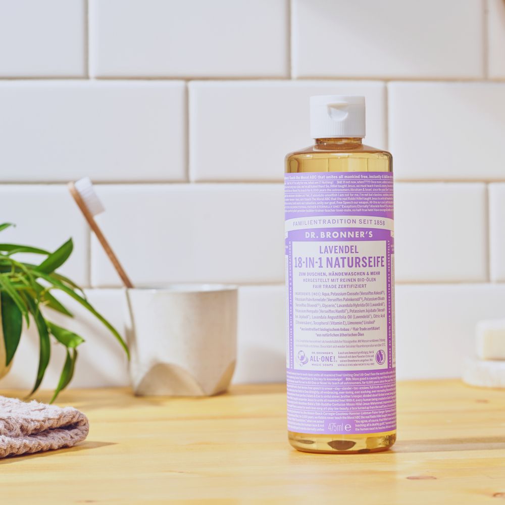 Sapone naturale Dr. Bronner's Lavanda in bagno. Flacone su superficie in legno. Sfondo: piastrelle e piante.
