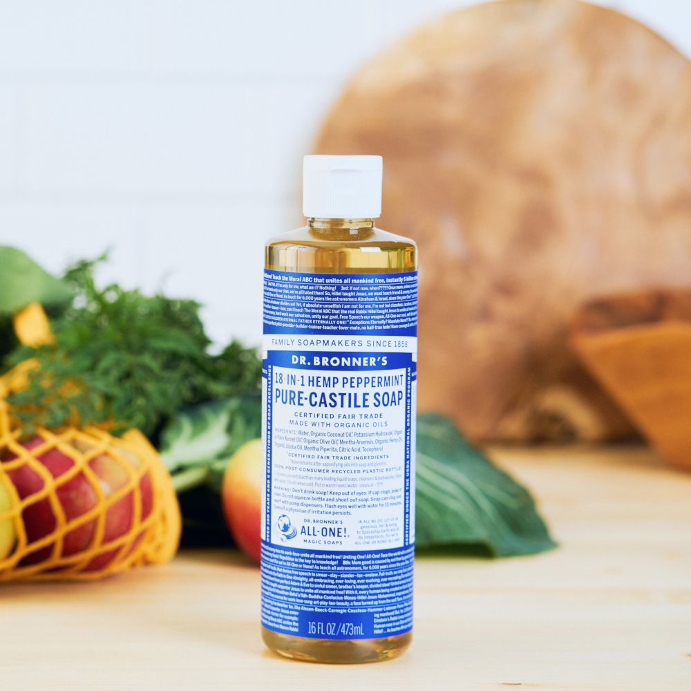 Una bottiglia di sapone liquido è appoggiata su un tavolo di legno. Verdure e frutta sullo sfondo.