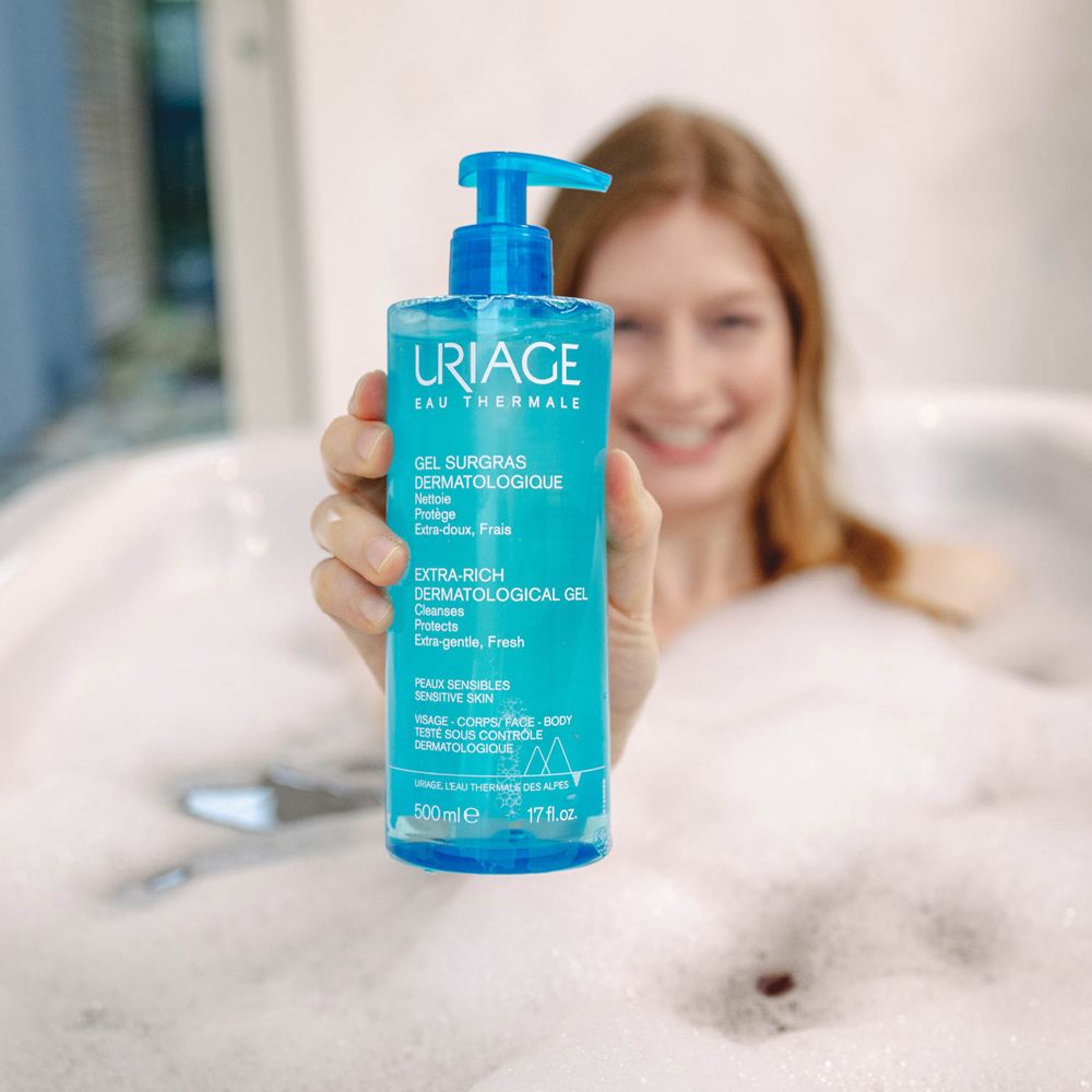 Femme dans un bain tenant Uriage Gel Surgras Dermatologique. Flacon bleu avec pompe.