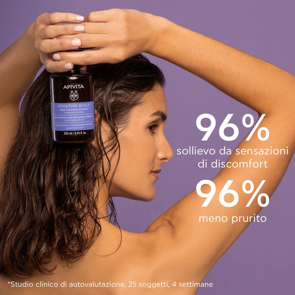 Donna con flacone di shampoo. Scritta: APIVITA, Sensitive Scalp Shampoo. Testo: 96% meno prurito.