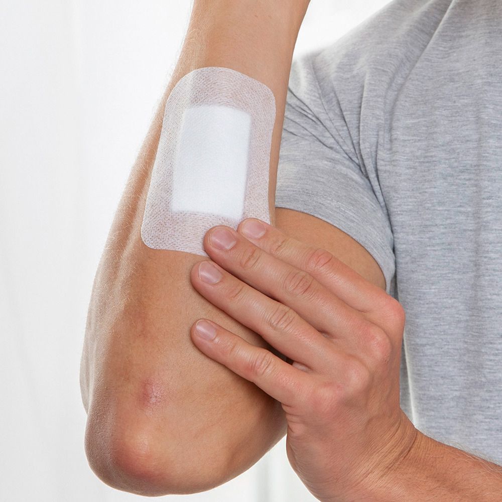 Arm mit angebrachtem Wundverband. Der Verband ist weiß und rechteckig.