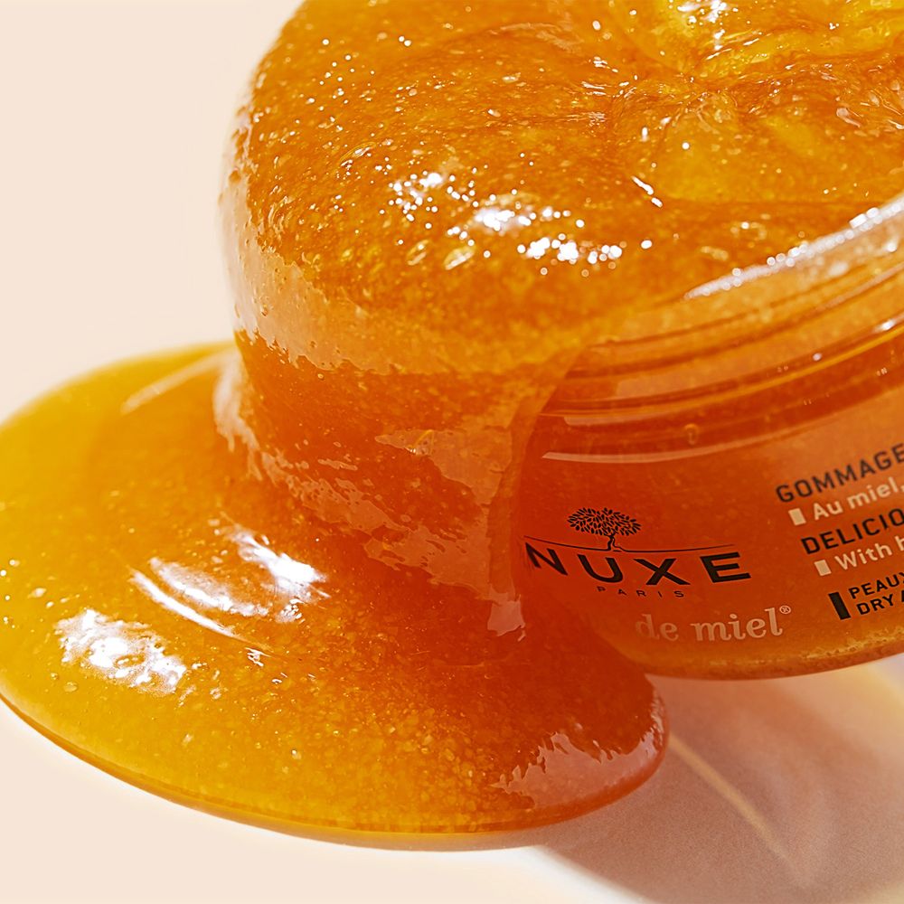 NUXE Rêve de Miel® Scrub Corpo. Scrub arancione che cola. Logo e testo: NUXE, Rêve de Miel.