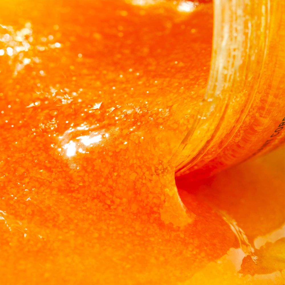 NUXE Rêve de Miel® Scrub Corpo. Scrub arancione che cola. Primo piano.
