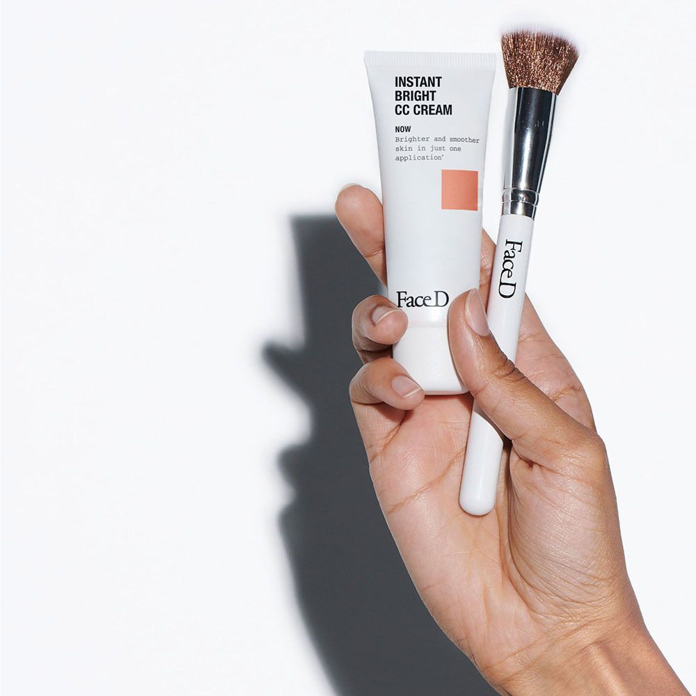 Hand hält FACE D CC Cream Tube und Make-up Pinsel. Weißer Griff, braune Borsten. Produktname sichtbar.