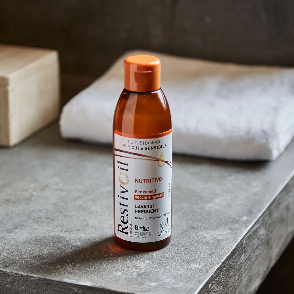 Restivoil Shampoo-Flasche auf einer Oberfläche. Braune Flasche mit orangefarbenem Deckel, neben einem Handtuch.