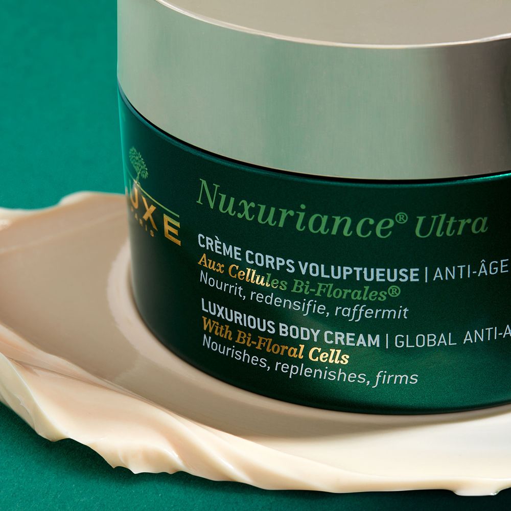 Primo piano di un vaso verde con coperchio argentato. Crema su una superficie bianca. Scritta Nuxuriance Ultra.