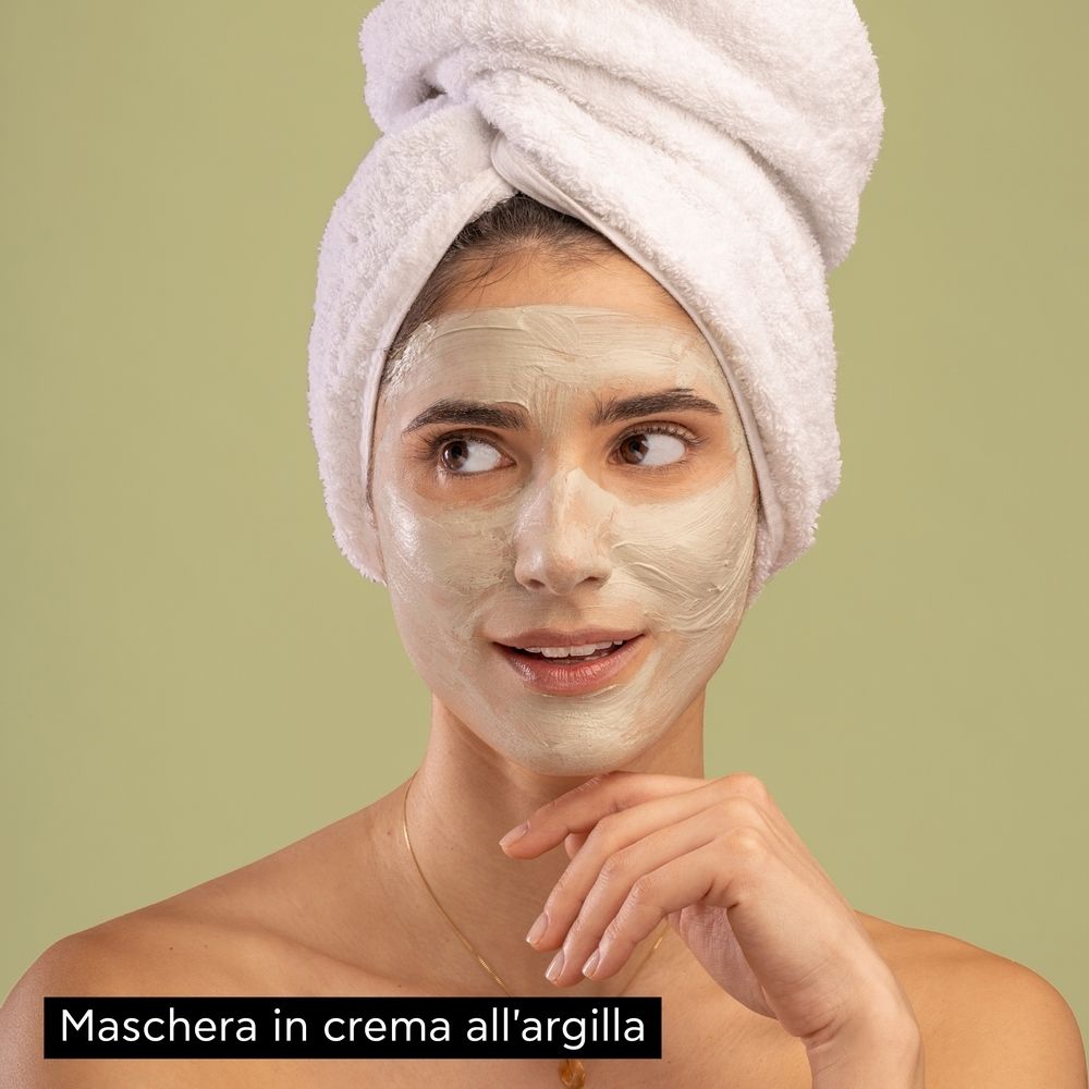 Donna con maschera viso. Viso coperto di argilla verde. Asciugamano sulla testa. Marchio APIVITA.