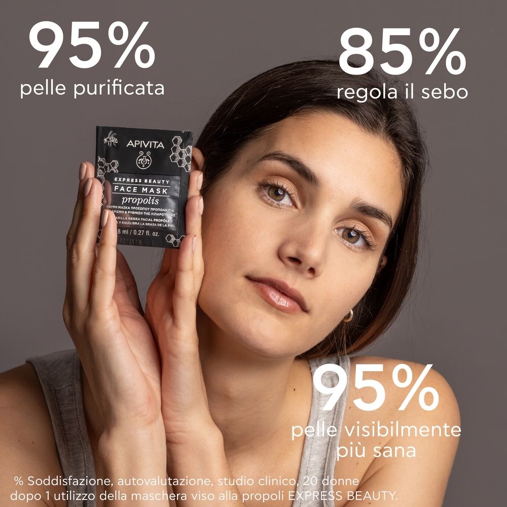 Frau hält APIVITA EXPRESS BEAUTY FACE MASK Propolis-Verpackung. Text: 95% pelle purificata, 85% regola il sebo, 95% pelle visibilmente più sana.