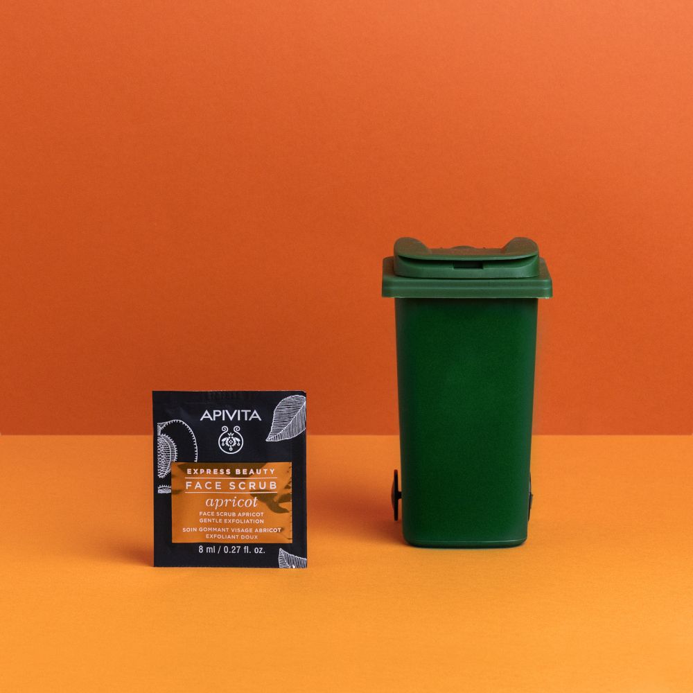 Confezione del prodotto accanto a un bidone della spazzatura verde. Scritto: APIVITA EXPRESS BEAUTY FACE SCRUB apricot.