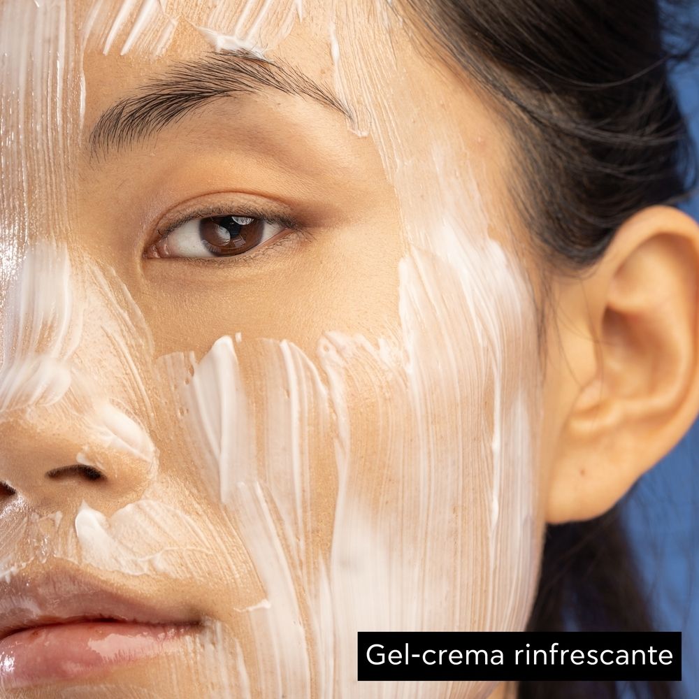 Primo piano di un viso coperto di crema bianca. Testo: Gel-crema rinfrescante.
