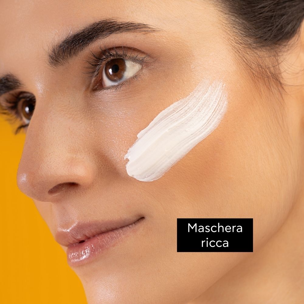 Viso di donna con crema sulla guancia. Testo: Maschera ricca.