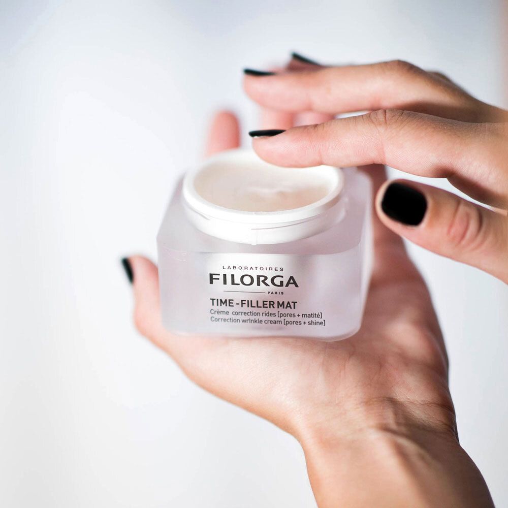 Mani che tengono un vasetto aperto FILORGA TIME-FILLER MAT. Crema visibile. Testo: Crème correction rides [pores + matité].