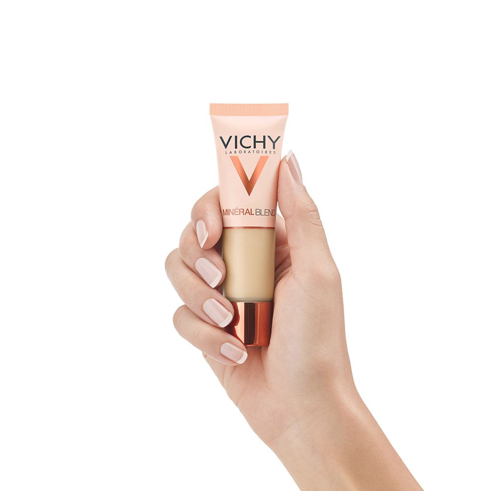 Main tenant un tube de fond de teint Vichy Mineralblend Nr. 01. Tube beige clair, base cuivrée. Logo visible.