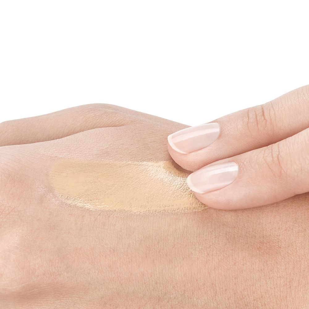 Mano con liquido beige applicato. Il liquido viene steso con il dito.